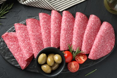 Photo of Slices of delicious sausage with olives and tomatoes served on black table, top view