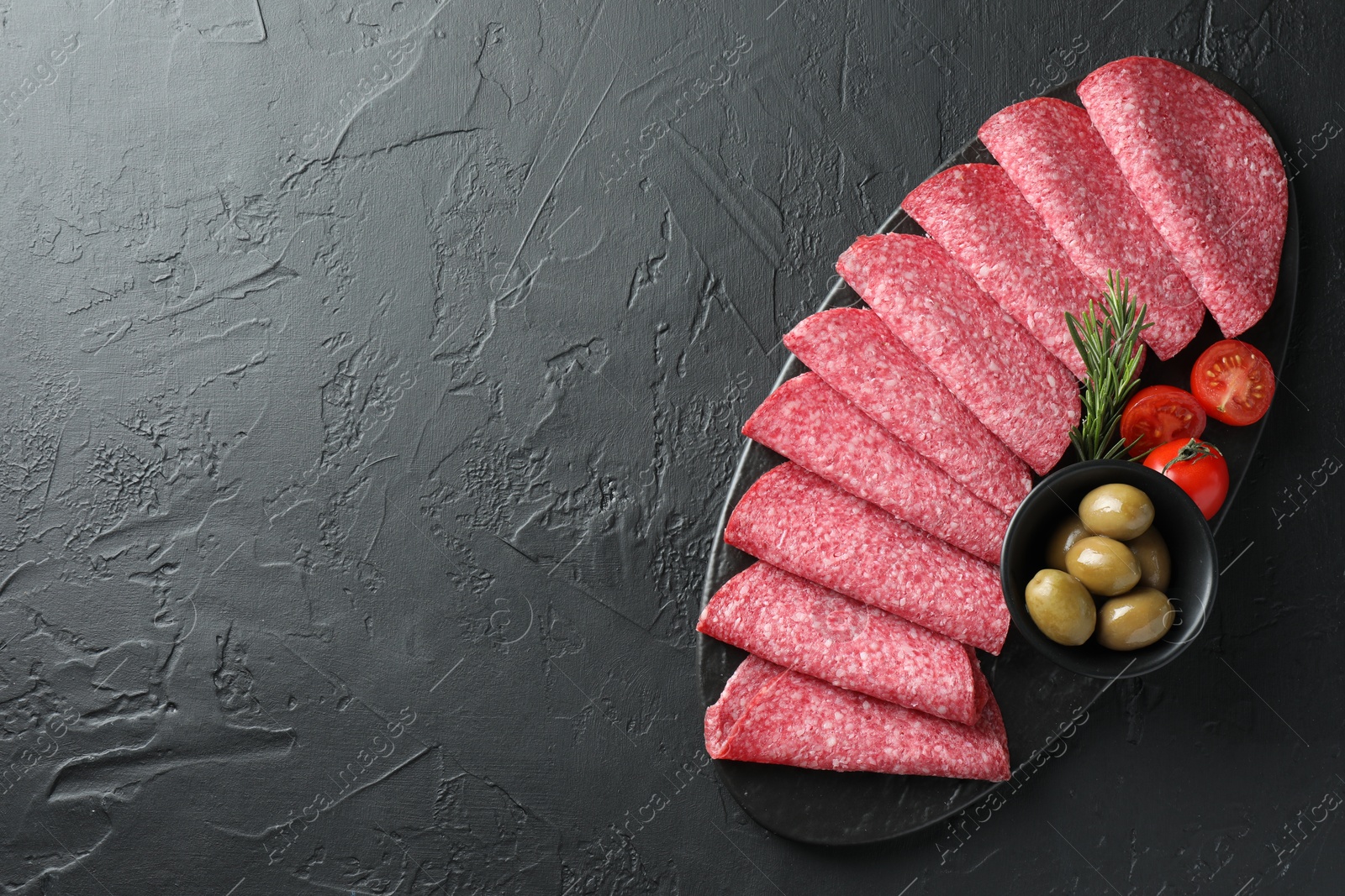 Photo of Slices of delicious sausage with olives and tomatoes served on black table, top view. Space for text