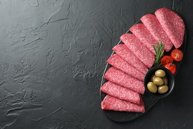 Photo of Slices of delicious sausage with olives and tomatoes served on black table, top view. Space for text
