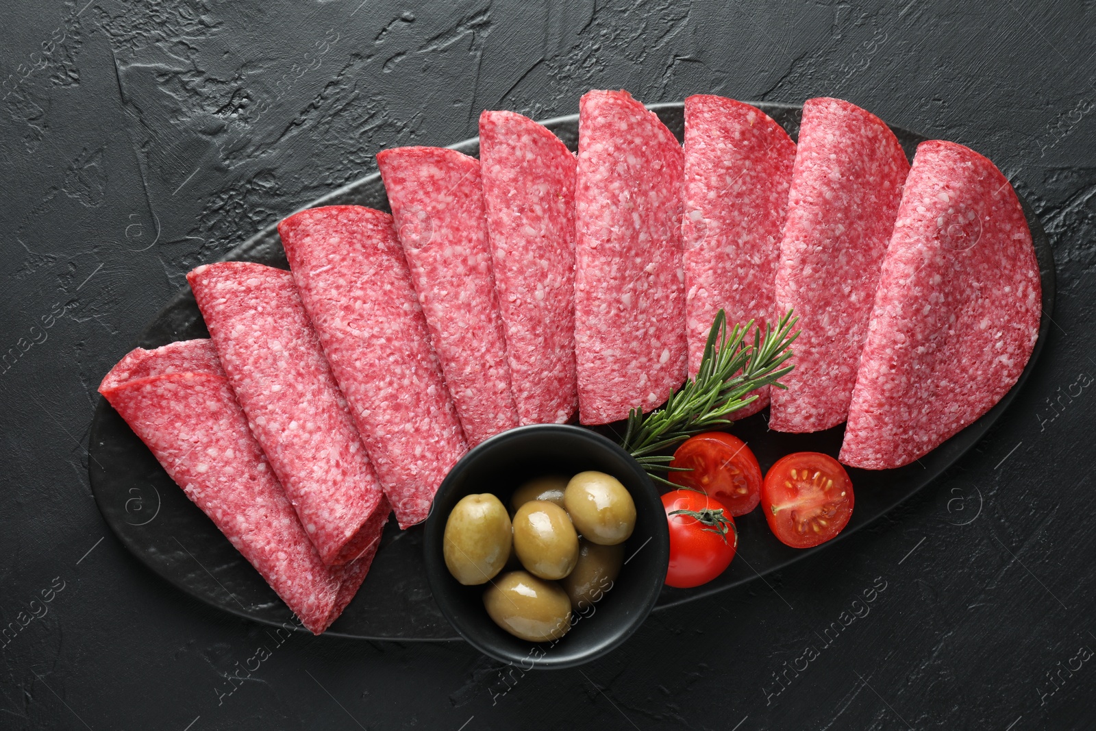 Slices of delicious sausage with olives and tomatoes served on black table, top view Photo of Slices of delicious sausage with olives and tomatoes served on black table, top view