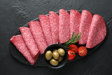 Photo of Slices of delicious sausage with olives and tomatoes served on black table, top view