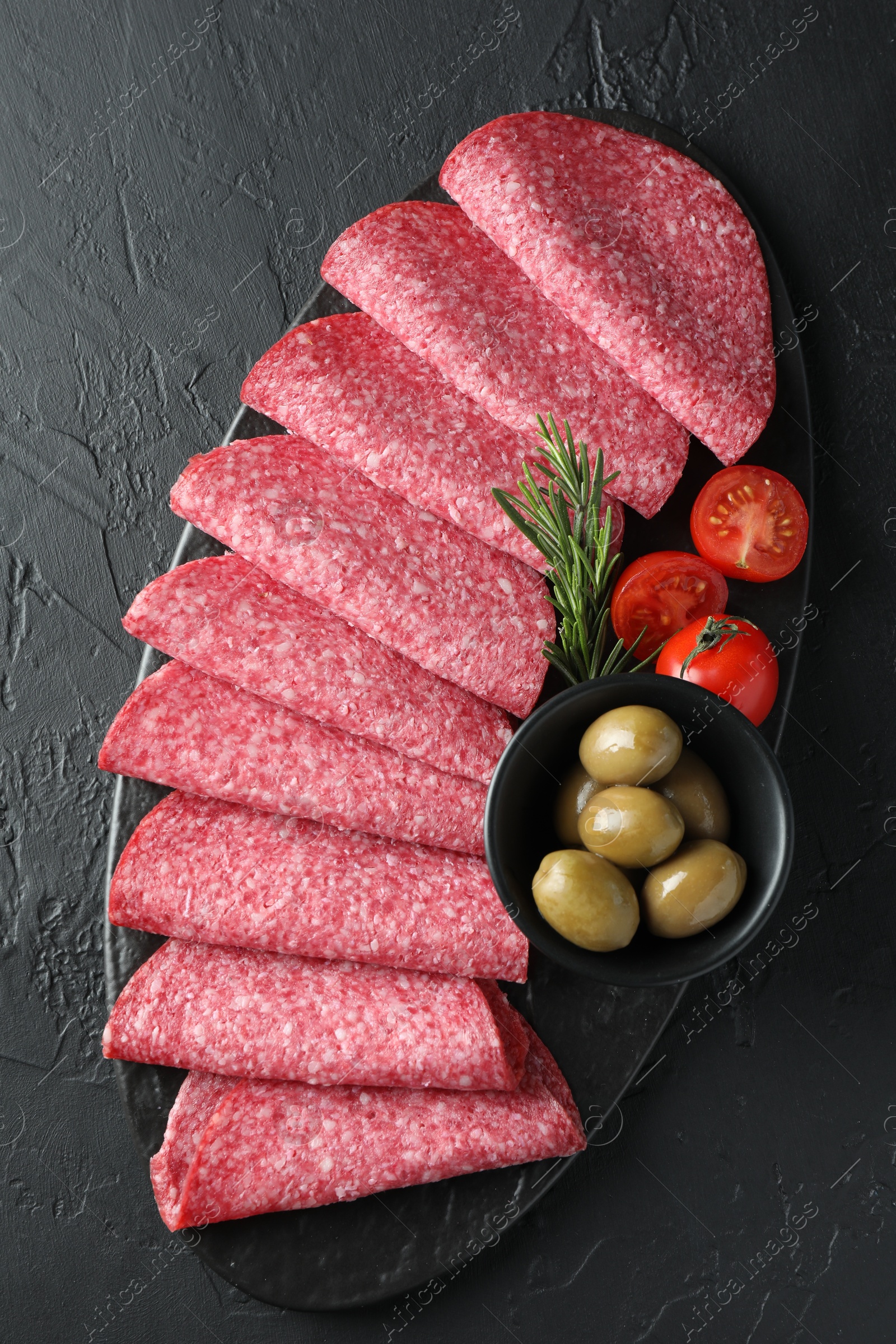 Slices of delicious sausage with olives and tomatoes served on black table, top view Photo of Slices of delicious sausage with olives and tomatoes served on black table, top view