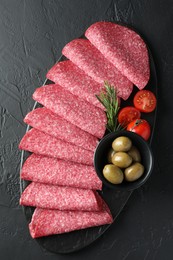 Photo of Slices of delicious sausage with olives and tomatoes served on black table, top view