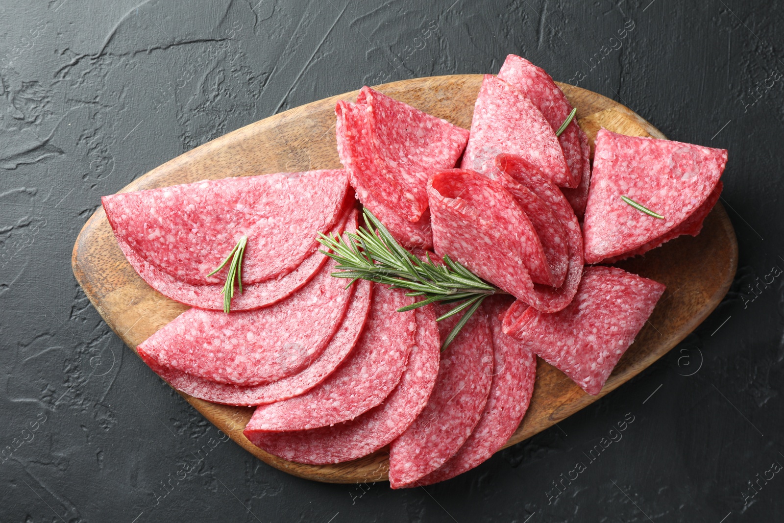 Slices of delicious sausage with rosemary served on black table, top view Photo of Slices of delicious sausage with rosemary served on black table, top view