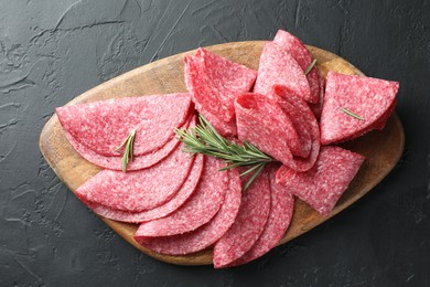 Photo of Slices of delicious sausage with rosemary served on black table, top view