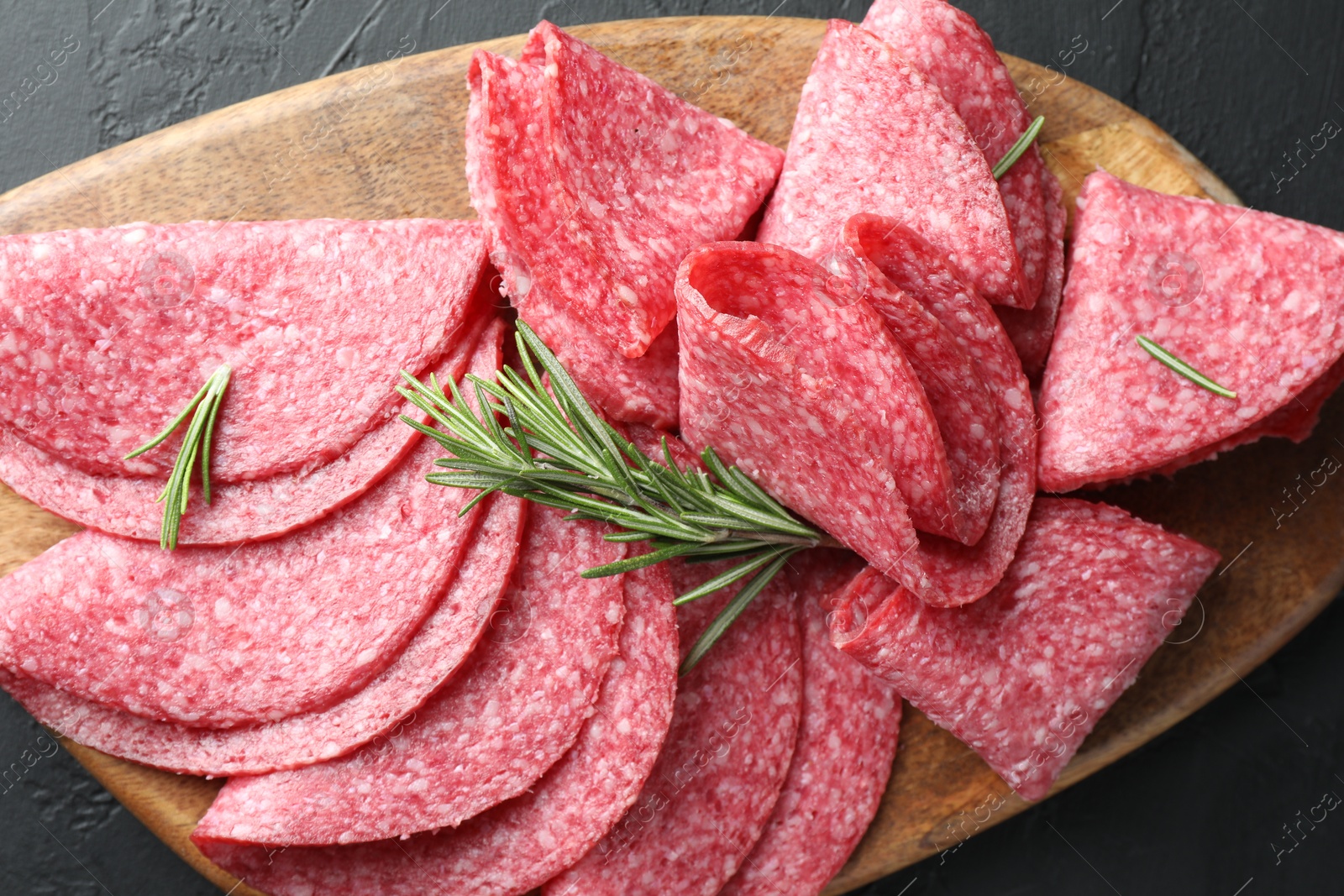 Photo of Slices of delicious sausage with rosemary served on black table, top view