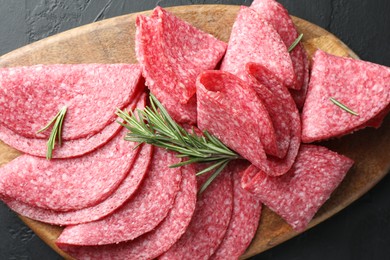 Photo of Slices of delicious sausage with rosemary served on black table, top view