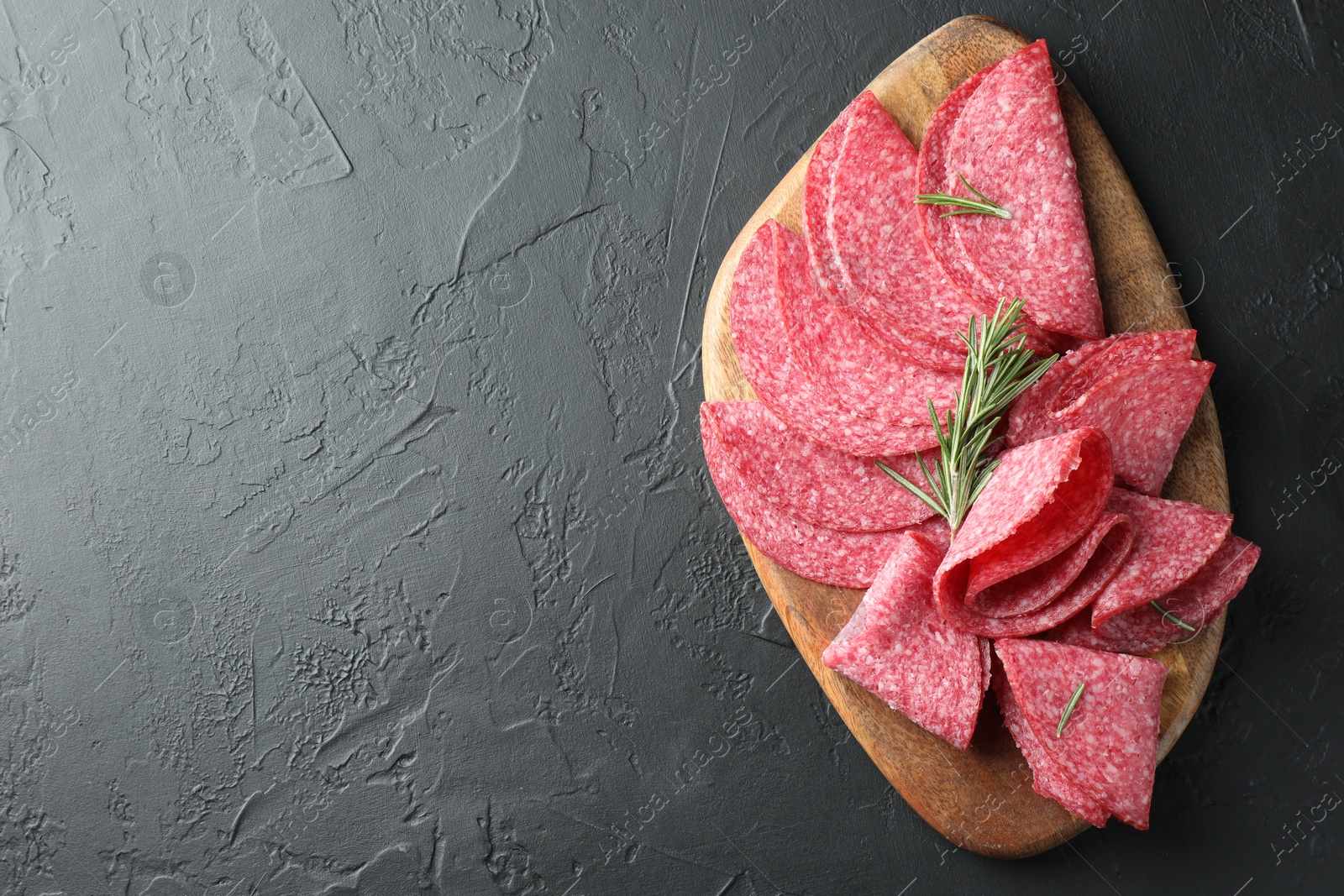 Photo of Slices of delicious sausage with rosemary served on black table, top view. Space for text