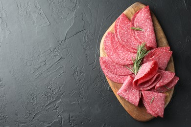 Photo of Slices of delicious sausage with rosemary served on black table, top view. Space for text
