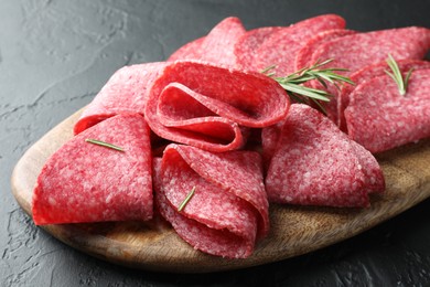 Photo of Slices of delicious sausage with rosemary served on black table, closeup