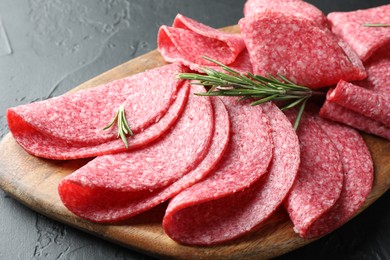 Photo of Slices of delicious sausage with rosemary served on black table, closeup