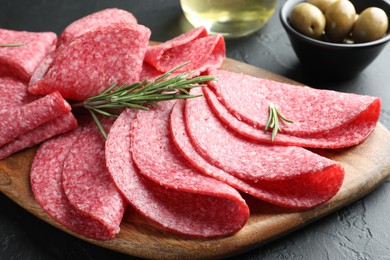 Photo of Slices of delicious sausage with rosemary served on black table, closeup