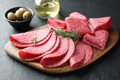 Photo of Slices of delicious sausage with rosemary served on black table, closeup