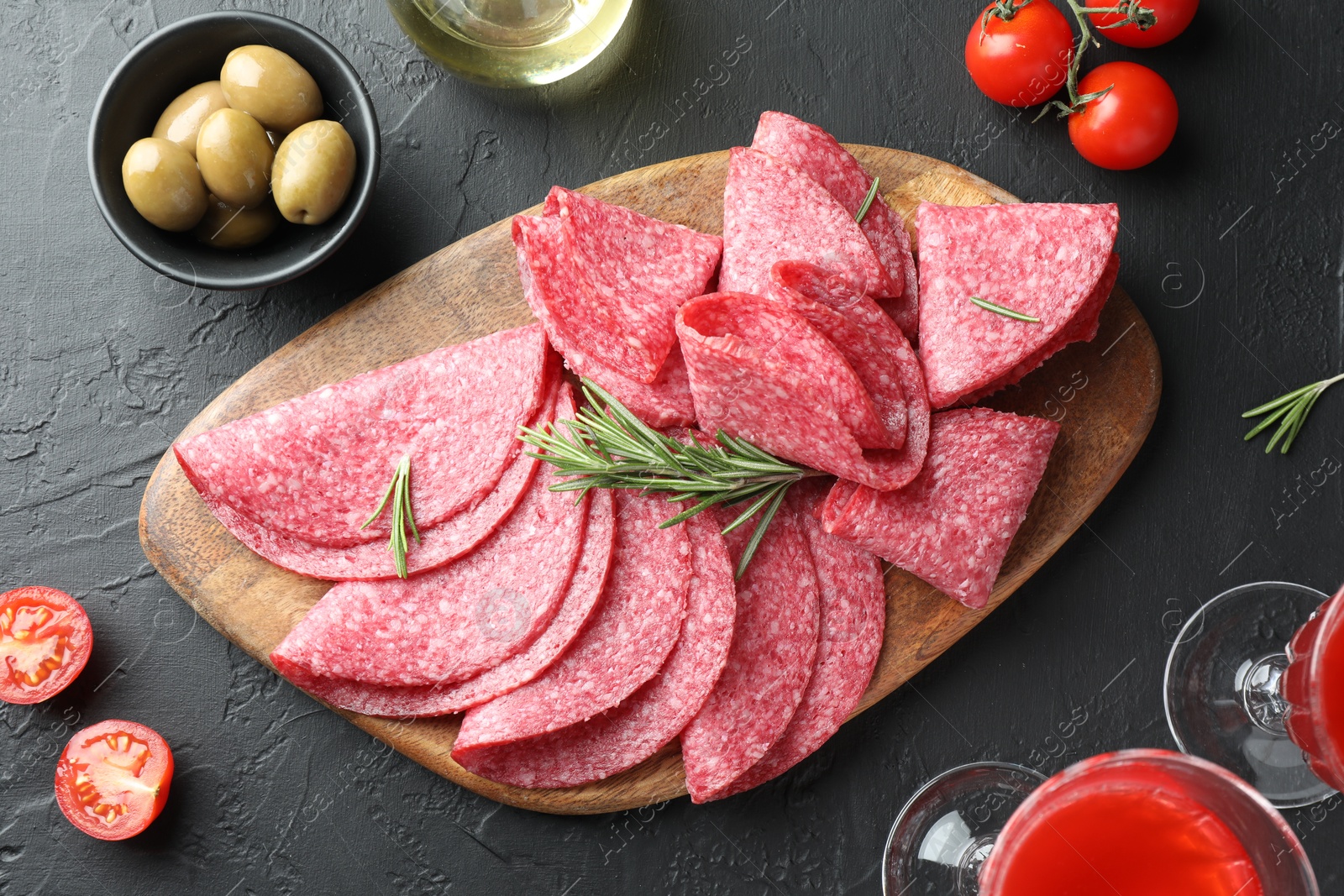 Slices of delicious sausage with rosemary served on black table, flat lay Photo of Slices of delicious sausage with rosemary served on black table, flat lay