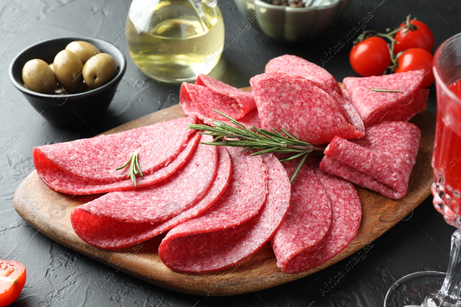Photo of Slices of delicious sausage with rosemary served on black table, closeup
