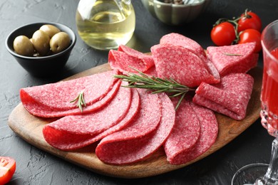 Photo of Slices of delicious sausage with rosemary served on black table, closeup