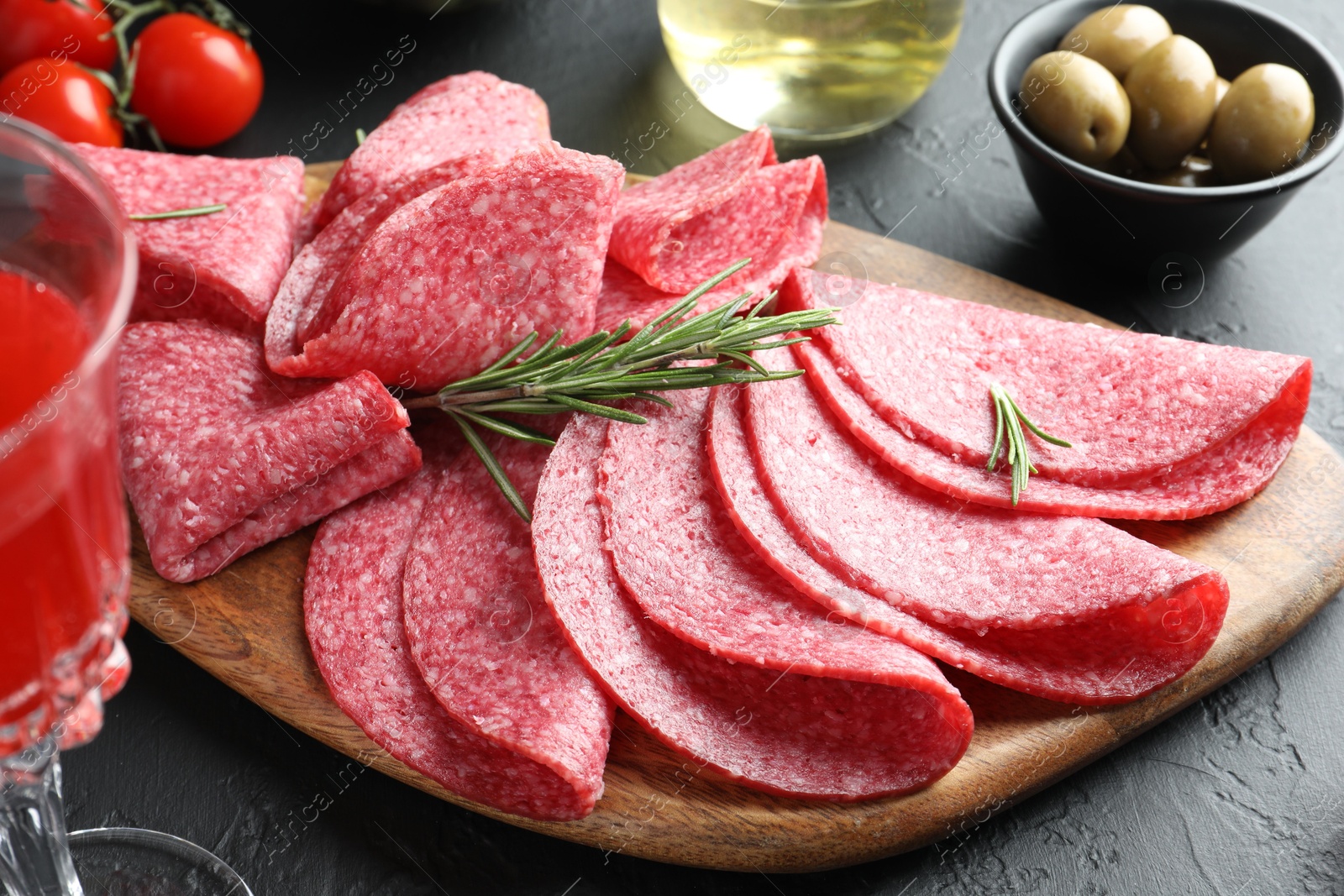 Photo of Slices of delicious sausage with rosemary served on black table, closeup