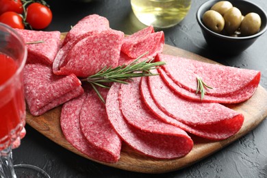 Photo of Slices of delicious sausage with rosemary served on black table, closeup