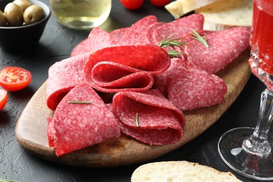 Photo of Slices of delicious sausage with rosemary served on black table, closeup