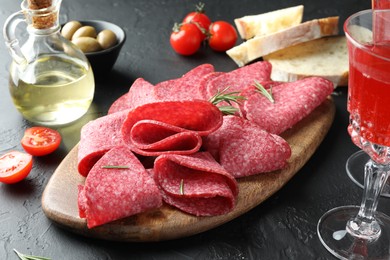 Photo of Slices of delicious sausage with rosemary served on black table, closeup