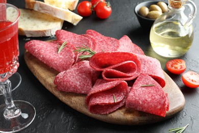 Photo of Slices of delicious sausage with rosemary served on black table, closeup