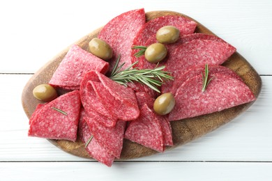 Photo of Slices of delicious sausage with olives and rosemary served on white wooden table, top view