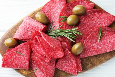 Photo of Slices of delicious sausage with olives and rosemary served on white wooden table, top view