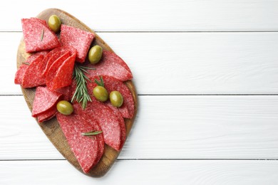 Photo of Slices of delicious sausage with olives and rosemary served on white wooden table, top view. Space for text