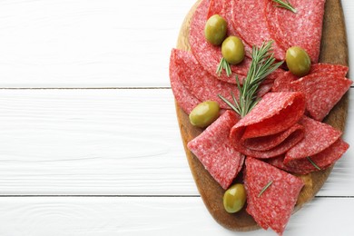 Photo of Slices of delicious sausage with olives and rosemary served on white wooden table, top view. Space for text