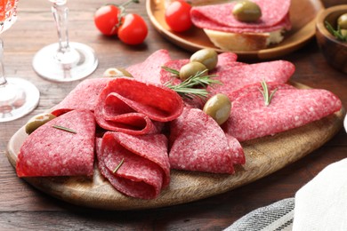 Photo of Slices of delicious sausage with olives and rosemary served on wooden table, closeup