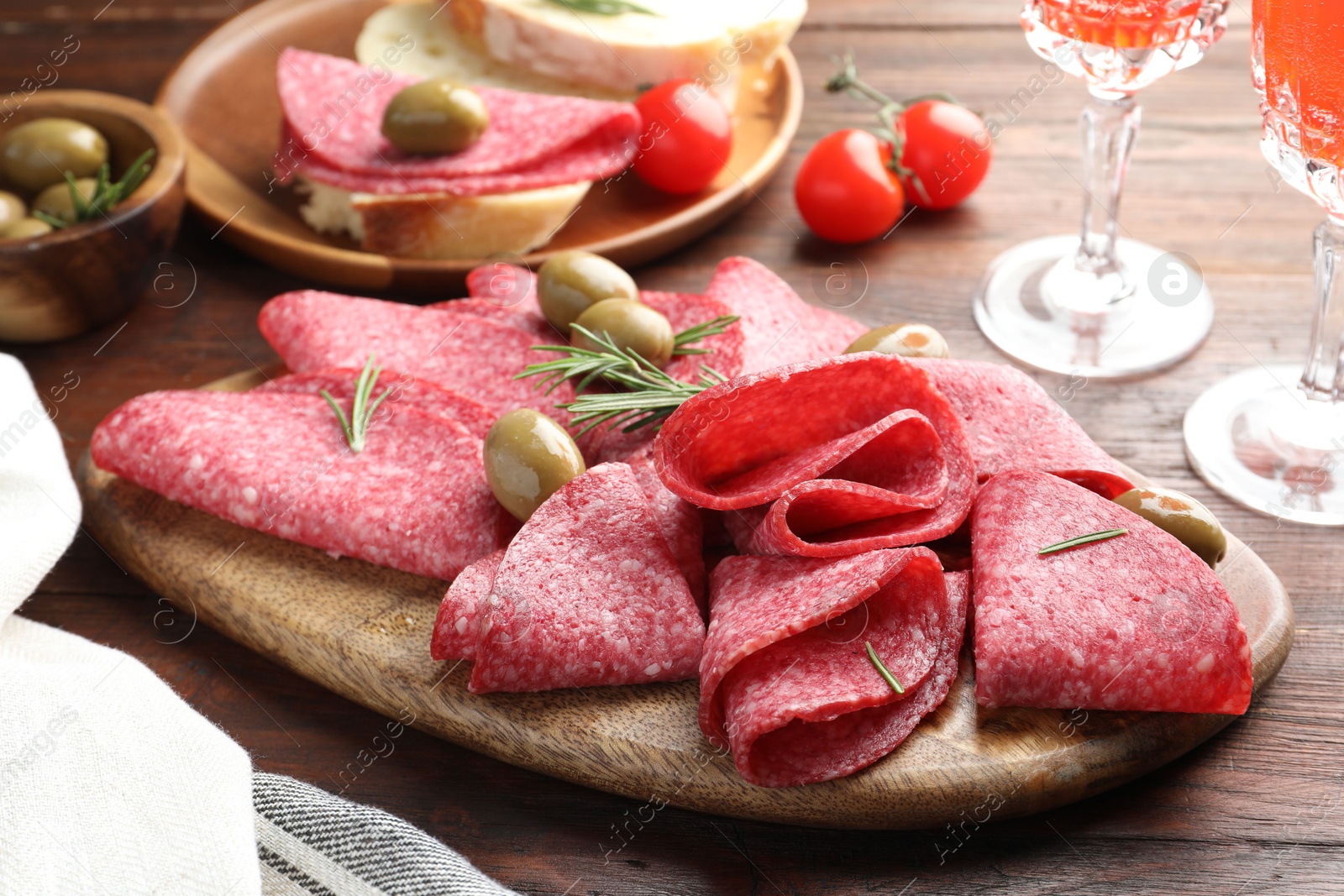 Slices of delicious sausage with olives and rosemary served on wooden table, closeup Photo of Slices of delicious sausage with olives and rosemary served on wooden table, closeup