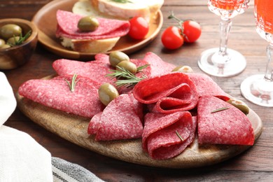 Photo of Slices of delicious sausage with olives and rosemary served on wooden table, closeup
