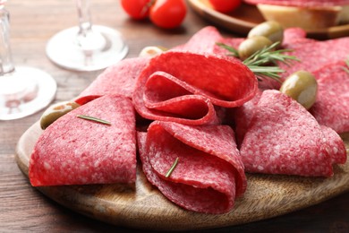 Photo of Slices of delicious sausage with olives and rosemary served on wooden table, closeup