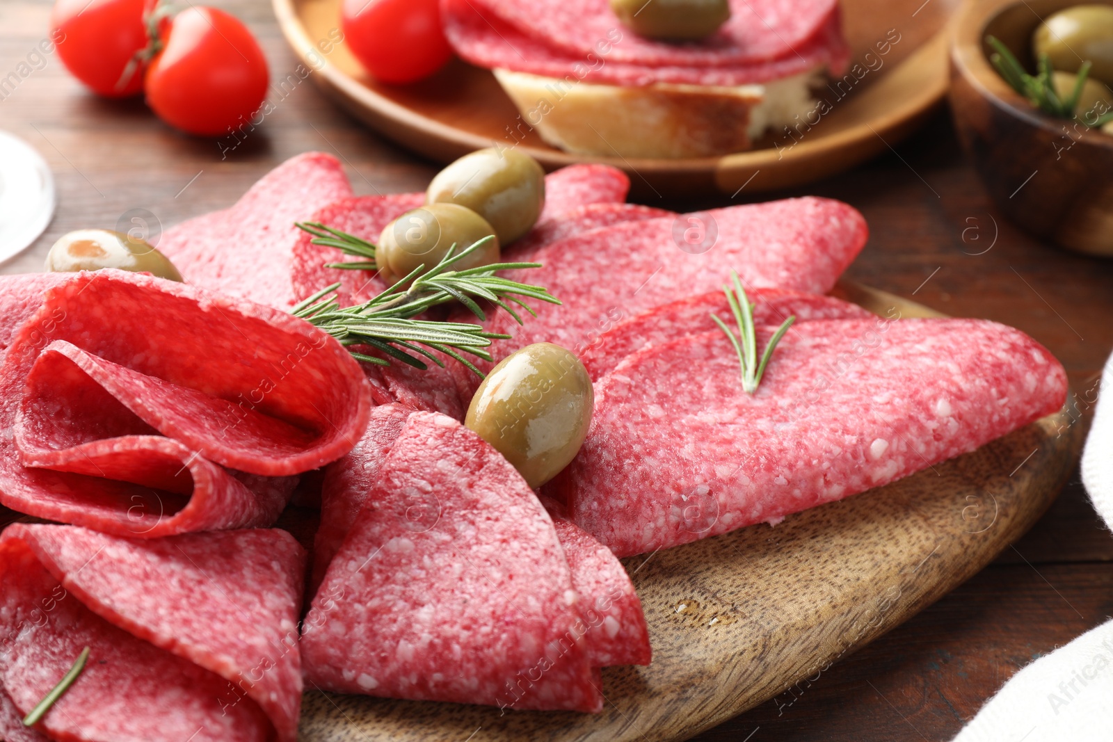 Slices of delicious sausage with olives and rosemary served on wooden table, closeup Photo of Slices of delicious sausage with olives and rosemary served on wooden table, closeup