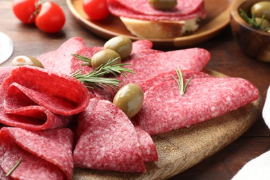 Photo of Slices of delicious sausage with olives and rosemary served on wooden table, closeup