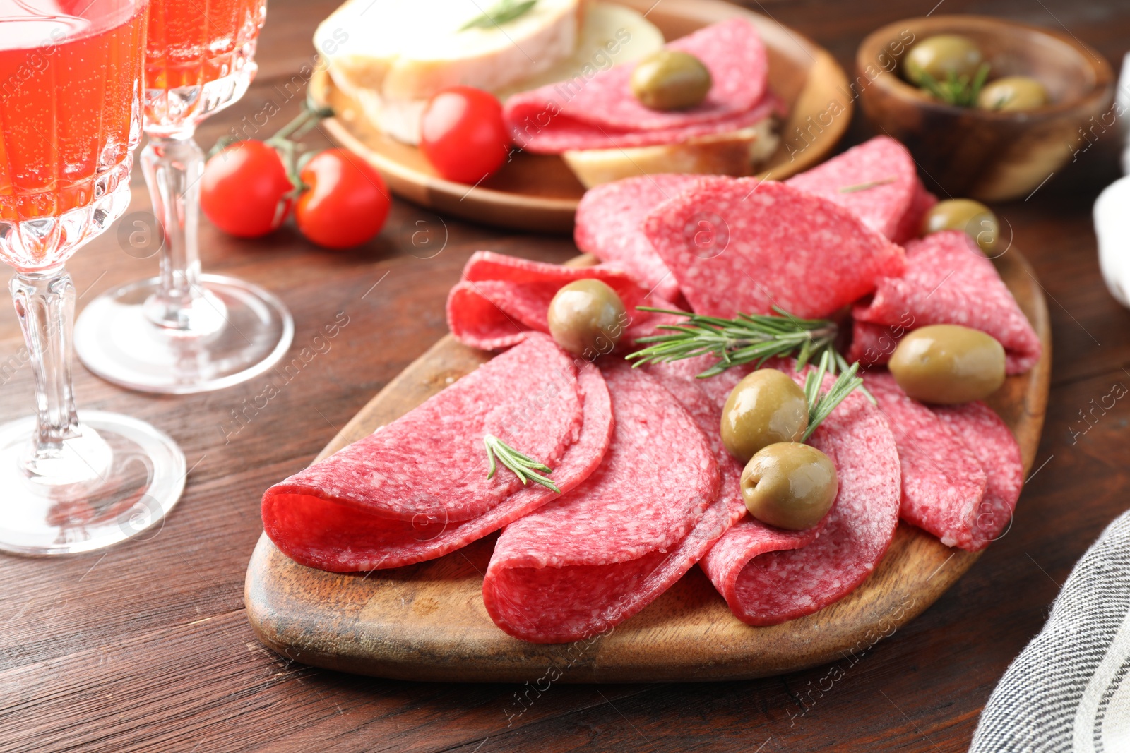 Photo of Slices of delicious sausage with olives and rosemary served on wooden table, closeup