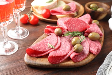 Photo of Slices of delicious sausage with olives and rosemary served on wooden table, closeup