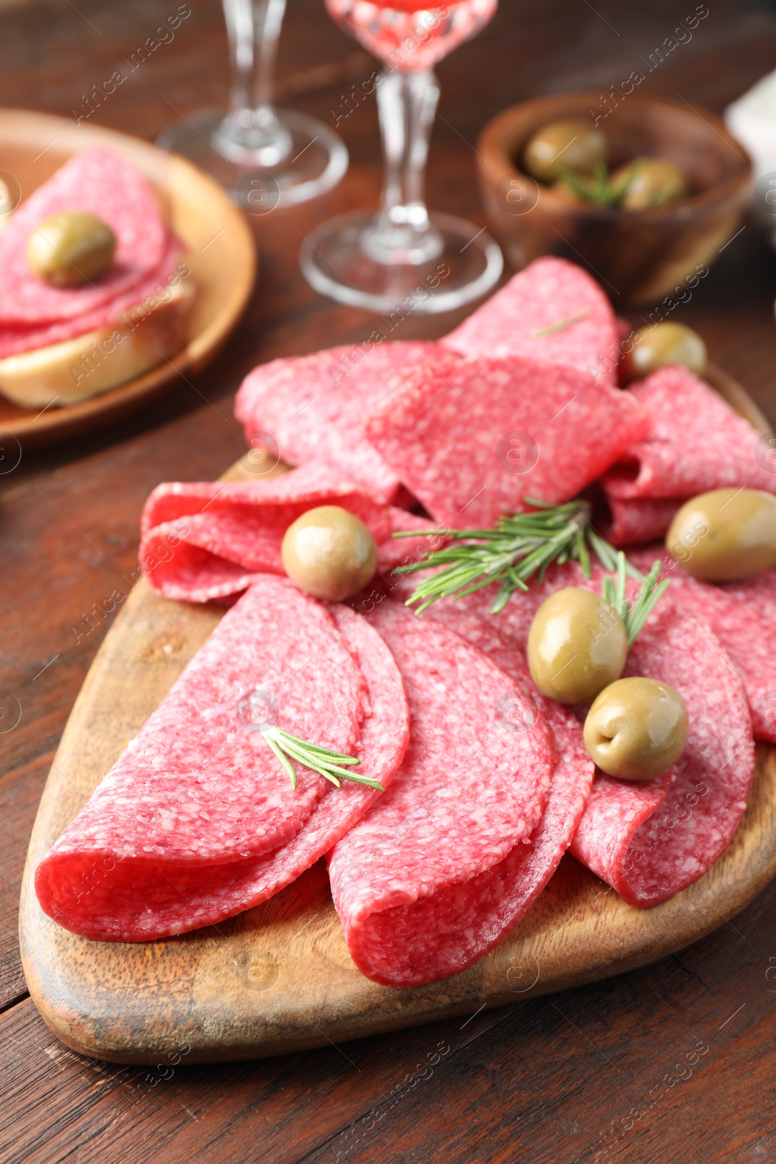 Photo of Slices of delicious sausage with olives and rosemary served on wooden table, closeup