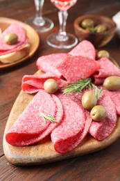 Photo of Slices of delicious sausage with olives and rosemary served on wooden table, closeup