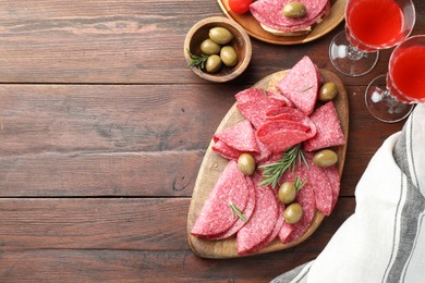 Photo of Slices of delicious sausage with olives and rosemary served on wooden table, flat lay. Space for text