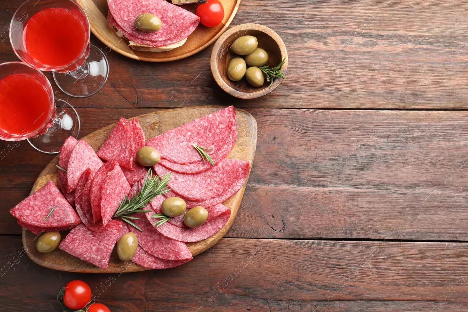 Photo of Slices of delicious sausage with olives and rosemary served on wooden table, flat lay. Space for text