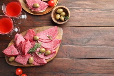 Photo of Slices of delicious sausage with olives and rosemary served on wooden table, flat lay. Space for text