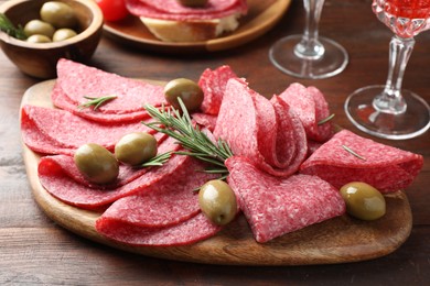 Photo of Slices of delicious sausage with olives and rosemary served on wooden table, closeup