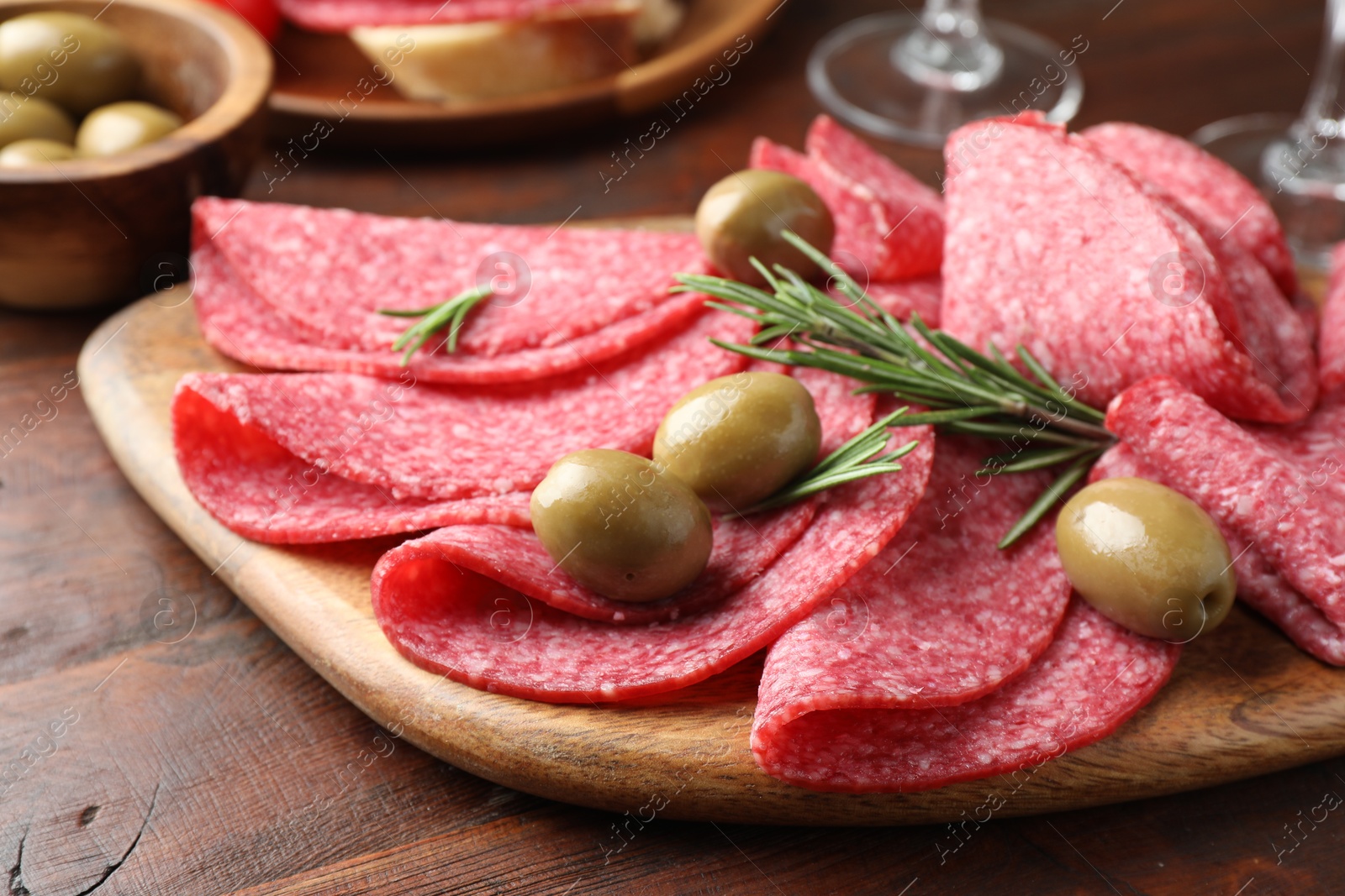 Photo of Slices of delicious sausage with olives and rosemary served on wooden table, closeup