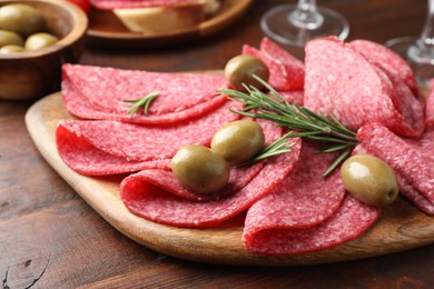 Photo of Slices of delicious sausage with olives and rosemary served on wooden table, closeup