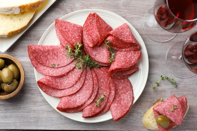 Photo of Slices of delicious sausage with thyme served on light wooden table, flat lay