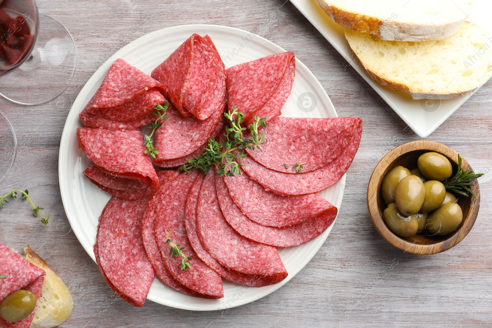 Photo of Slices of delicious sausage with thyme served on light wooden table, flat lay