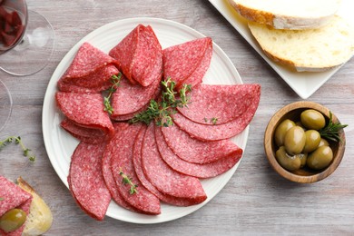 Photo of Slices of delicious sausage with thyme served on light wooden table, flat lay
