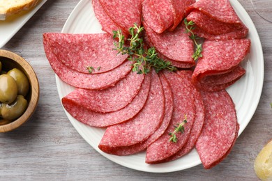Photo of Slices of delicious sausage with thyme served on light wooden table, flat lay