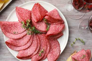 Photo of Slices of delicious sausage with thyme served on light wooden table, flat lay